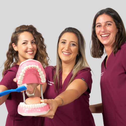 3 higienistas que trabajan en Sevilla Este la clínica dental Las Camelias enseñando un modelo de una boca y un cepillo de dientes.